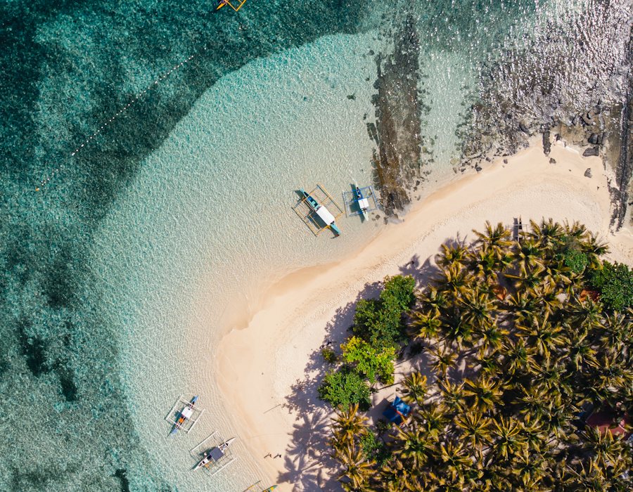 Aerial view of a sandy island with outrigger boats